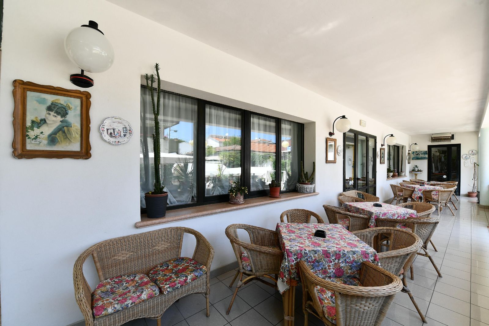 Veranda luminosa con poltroncine in vimini e tavoli fioriti